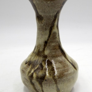 May include: A small, light brown ceramic vase with brown and white streaks and a narrow neck.