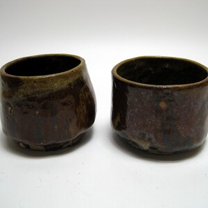 May include: Two brown ceramic cups with a textured glaze. The cups are slightly different shapes and sizes.