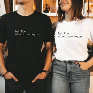 Op de afbeelding: Twee mensen dragen bijpassende T-shirts met de tekst "Let the adventure begin" erop gedrukt. De persoon links draagt een zwart T-shirt en de persoon rechts draagt een wit T-shirt.