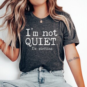 May include: A dark grey heather t-shirt with the text "I'm not QUIET... I'm plotting" printed in white.