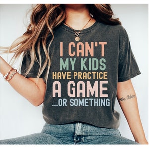 May include: A dark gray t-shirt with the text "I can't my kids have practice a game...or something" in colorful letters.