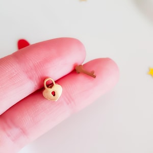 May include: A gold heart-shaped padlock with a keyhole and a matching gold key. The padlock and key are small and delicate, perfect for a charm bracelet or necklace.