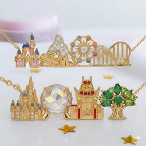 May include: Two gold necklaces with theme park designs. One features a castle, mountain, Ferris wheel, and roller coaster. The other has a castle, a large crystal, a theater, and a tree. Each necklace has a gold chain.