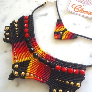 May include: A black macrame necklace with red and yellow beads and black crystals. The necklace is in the shape of a wide collar and has a matching pendant.