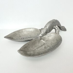May include: A silver-colored lobster-shaped serving dish. The dish is made of metal and features a detailed lobster design with two large, leaf-shaped serving areas. The lobster's body forms the handle.