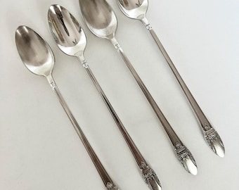 May include: Four silver spoons with long, slender handles and oval bowls are arranged diagonally. The spoons have a decorative design at the base of the bowl and the end of the handle. The spoons are set against a white background.