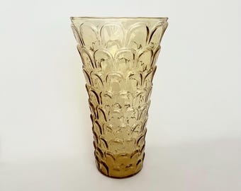 May include: Amber-colored glass vase with a textured, repeating pattern. The vase has a flared top and a cylindrical body. The design is reminiscent of overlapping scales. The vase is empty and sits on a white surface.