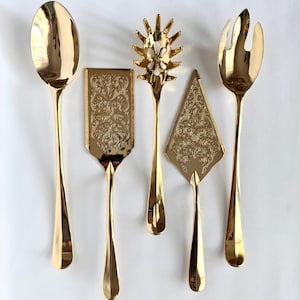May include: A set of five gold-toned serving utensils including a large spoon, a rectangular spatula with an embossed floral pattern, a spiky pasta server, a triangular cake server with an embossed floral pattern, and a three-pronged fork.