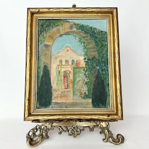 May include: A framed painting of a building with an archway covered in green vines. The painting is on a gold easel with ornate details. The painting is signed "D. Norman - 34".