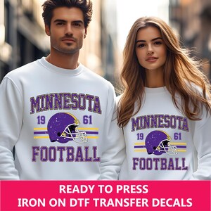 May include: White sweatshirt with a purple and yellow Minnesota Football design. The design includes a football helmet with a distressed look and the years 19 and 61.