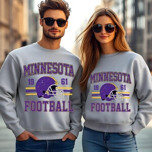 May include: Two grey sweatshirts with a purple and yellow Minnesota Football design. The design features a football helmet with the numbers 19 and 61.