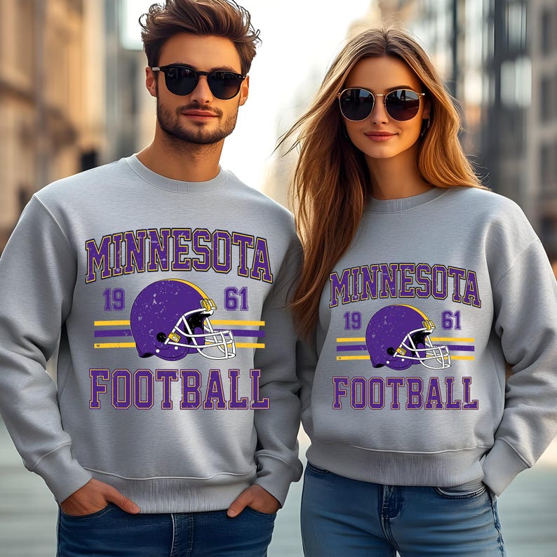 May include: Two grey sweatshirts with a purple and yellow Minnesota Football design. The design features a football helmet with the numbers 19 and 61.