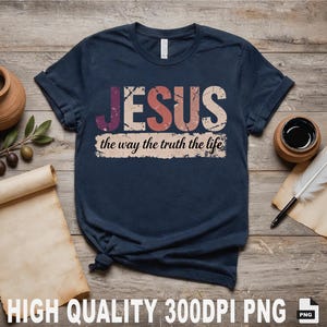 Peut inclure: T-shirt bleu marine avec le mot "JESUS" en lettres usées, sur la phrase "the way the truth the life". Le t-shirt est posé sur une surface en bois avec une bougie, une branche d'olivier et un parchemin.