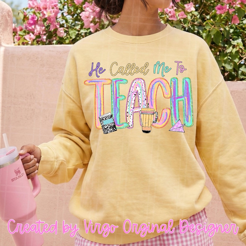 May include: A pale yellow crewneck sweatshirt featuring the text "He Called Me To TEACH" in a colorful, multi-toned font. The design includes graphic illustrations of a black and white composition notebook, a pencil, and a paper airplane.