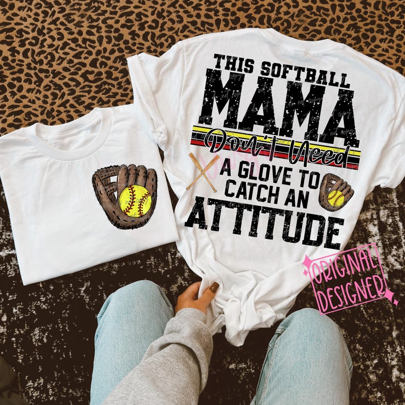 K&ouml;nnte beinhalten: Wei&szlig;es T-Shirt mit dem Text "This Softball Mama Don't Need A Glove To Catch An Attitude" in Schwarz und Rot. Das Shirt hat eine Grafik eines Baseballhandschuhs und eines Balls.
