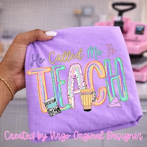 May include: A light purple t-shirt featuring the text "He Called Me To TEACH" in colorful, multi-toned lettering. The design includes a black and white composition notebook, a yellow pencil cup, and a small purple paper airplane graphic.