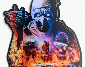 May include: A sticker featuring a menacing clown with a top hat, set against a fiery background. The sticker has the text "TERRIFIER 2" in red, with the film's title and a carnival scene. The clown's face is white and blue.