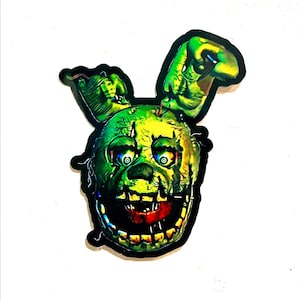 May include: A green and yellow animatronic character with a large, toothy grin. The character has a torn and tattered appearance, with exposed wires and a missing eye. The character's head is tilted to the side, and its eyes are wide with a menacing expression.