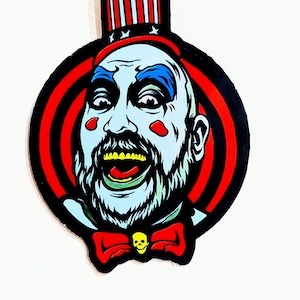May include: A cartoon illustration of a man with a blue face, red and white striped hat, and a red bow tie with a skull. The background is a red and black target.