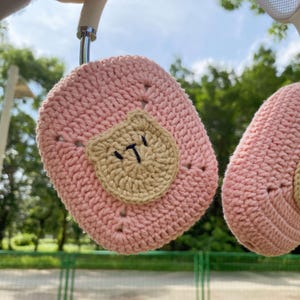 Pu&ograve; includere: Due custodie per AirPod in crochet rosa con una toppa in crochet marrone su una custodia che dice "IT".