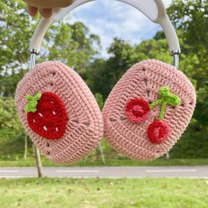 May include: Pink crocheted headphone covers with a strawberry and cherry design.