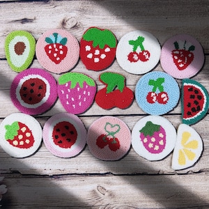 May include: A set of 14 colorful round needle felted coasters featuring various fruit designs, including strawberries, cherries, watermelon, lemons, and a single avocado.