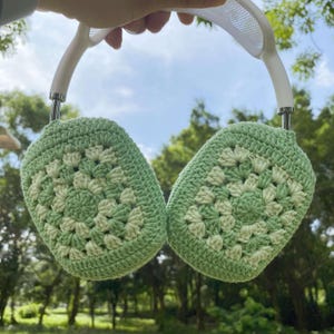 Puede incluir: Orejeras de ganchillo verde con una diadema blanca. Las orejeras están hechas con un patrón de punto de granny square.