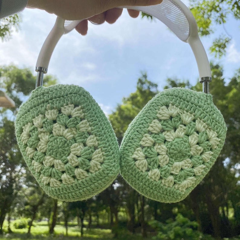 K&ouml;nnte beinhalten: Gr&uuml;ne geh&auml;kelte Ohrensch&uuml;tzer mit einem wei&szlig;en Kopfband. Die Ohrensch&uuml;tzer sind mit einem Granny-Square-Stichmuster gearbeitet.