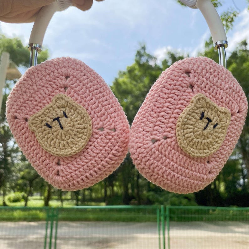 Pu&ograve; includere: Copri cuffie in crochet rosa con un viso di orso in crochet marrone su ogni lato.