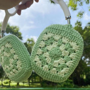 K&ouml;nnte beinhalten: Gr&uuml;ne und wei&szlig;e geh&auml;kelte Ohrensch&uuml;tzer mit einem wei&szlig;en Stirnband. Die Ohrensch&uuml;tzer sind mit einem Granny-Square-Stich gearbeitet.
