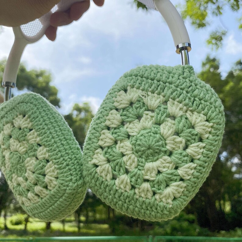 K&ouml;nnte beinhalten: Gr&uuml;ne und wei&szlig;e geh&auml;kelte Ohrensch&uuml;tzer mit einem wei&szlig;en Stirnband. Die Ohrensch&uuml;tzer sind mit einem Granny-Square-Stich gearbeitet.