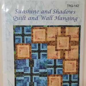 May include: A quilt pattern titled "Sunshine and Shadows" with a geometric design. The quilt features squares in shades of blue, tan, and brown. The finished quilt size is 72 inches square, and the wall hanging size is 24 inches.