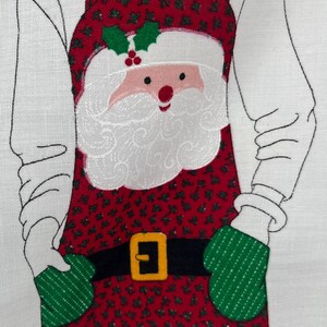 May include: A Christmas-themed apron featuring a Santa Claus design. The apron is red with a pattern of green holly leaves and berries. Santa's face, beard, and hat are white and pink. The apron has a black belt with a gold buckle and green oven mitts.