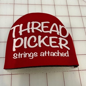 May include: Red thread picker with white text that reads "THREAD PICKER strings attached".
