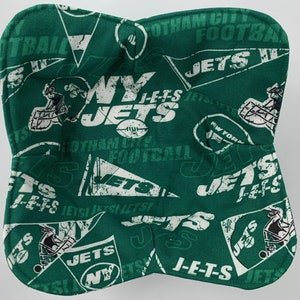 May include: A green and white fabric bowl cozy featuring the New York Jets football team logo and text. The design includes football helmets, pennants, and the words "JETS" and "Gotham City Football".