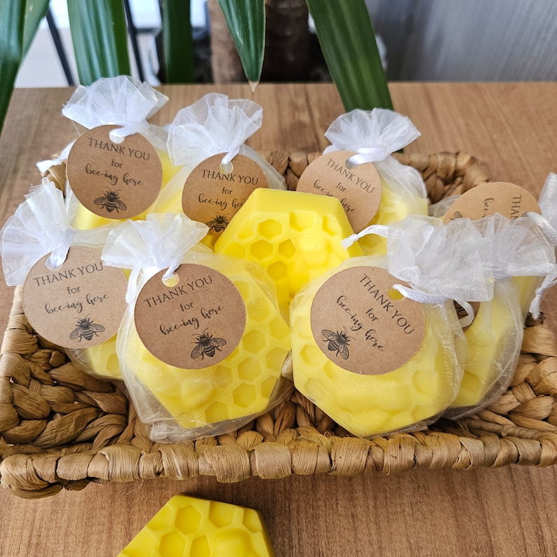 May include: A basket filled with small, yellow honeycomb-shaped soaps wrapped in white tulle bags. Each bag has a brown tag with the text "Thank You for bee-ing here" and a small bee illustration.