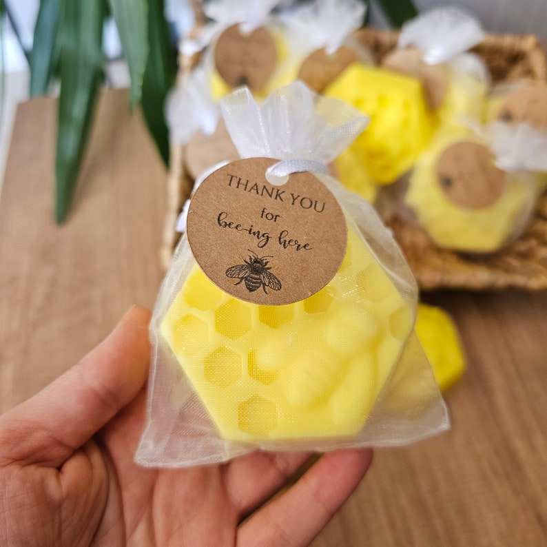 May include: A yellow honeycomb-shaped candle in a clear organza bag with a brown tag that says "Thank you for bee-ing here" with a small bee illustration.
