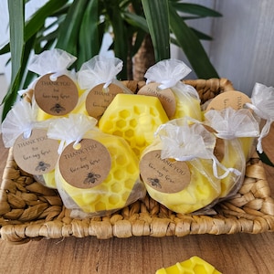 May include: A basket filled with small yellow honeycomb-shaped candles wrapped in white tulle bags with brown paper tags that say "Thank you for bee-ing here".
