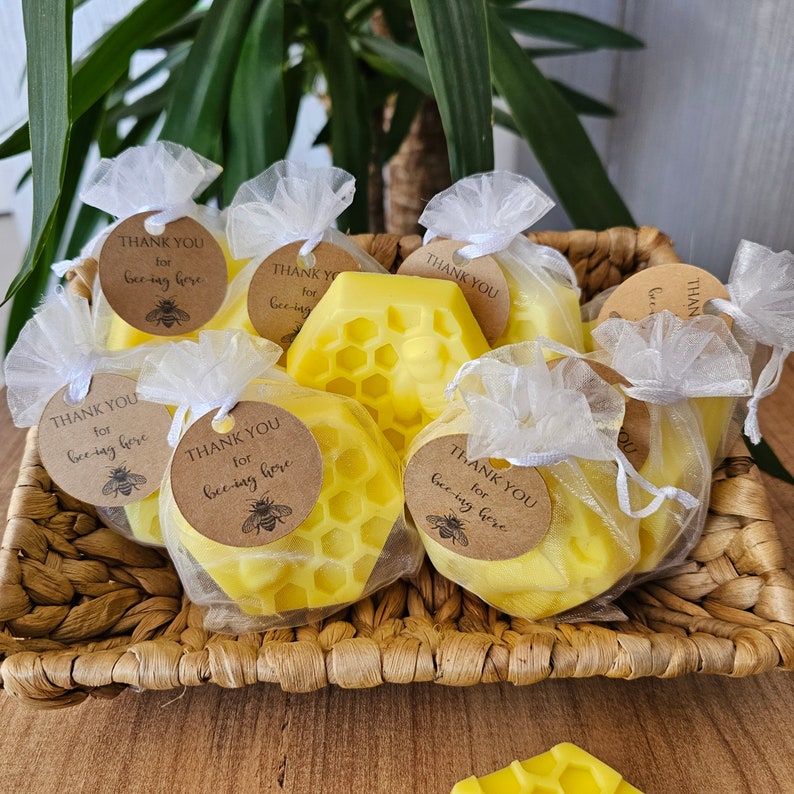 May include: A basket filled with small yellow honeycomb-shaped candles wrapped in white tulle bags with brown paper tags that say "Thank you for bee-ing here".