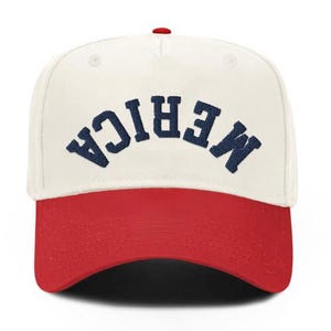 May include: A baseball cap with a white crown and a red brim. The word "MERICA" is embroidered in navy blue across the front. The cap has a red button on top.