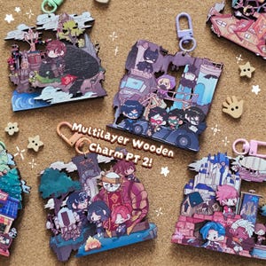 May include: A collection of colorful, multilayer wooden charms with various cartoon character designs. The charms feature images of characters, buildings, and vehicles. The text "Multilayer Wooden Charm PT 2!" is visible. Each charm has a metal clasp for attachment.