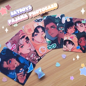 Puede incluir: Un conjunto de cuatro tarjetas coleccionables rectangulares tituladas BATBOYS PAJAMA PHOTOCARD, con ilustraciones estilo anime de personajes en pijama de animales. Las tarjetas muestran arte colorido con varias expresiones, pegatinas pequeñas y un pequeño dije con forma de caramelo.