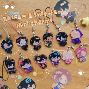 May include: A collection of acrylic mini charms featuring various illustrated characters with colourful lanyards and metal clasps. The text "BatFam & Superfam Mini Charms" is printed in the centre. Each charm depicts a unique character design.