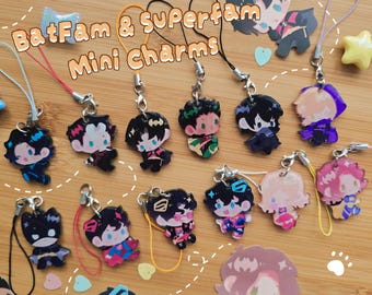 Peut inclure: Une collection de mini breloques en acrylique représentant divers personnages illustrés avec des cordons colorés et des fermoirs en métal. Le texte "BatFam & Superfam Mini Charms" est imprimé au centre. Chaque breloque présente un design unique.