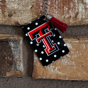 May include: A black and white keychain with a red and white "T" on it. The keychain has white polka dots and a red tassel.