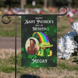 May include: A green garden flag with a shamrock design and a rainbow. The flag reads "Happy Saint Patrick's Day in Heaven" and has a photo of a woman and the name "Megan".