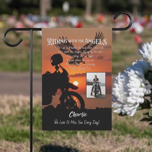 Può includere: Una bandiera da giardino in bianco e nero con una silhouette di un motociclista su uno sfondo di tramonto. La bandiera ha il testo "Riding with the Angels" e una poesia su un motociclista scomparso. La bandiera ha anche una foto di un uomo su una moto e il nome "Charlie" in basso. Il testo in basso dice "We Love & Miss You Every Day!"