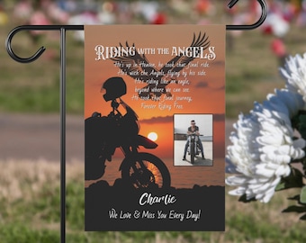 May include: A black and white garden flag with a silhouette of a motorcycle rider against a sunset background. The flag has the text "Riding with the Angels" and a poem about a motorcycle rider who has passed away. The flag also has a photo of a man on a motorcycle and the name "Charlie" at the bottom. The text at the bottom reads "We Love & Miss You Every Day!"