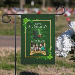 May include: Green garden flag with a gold frame and shamrocks. The flag says "Happy St. Patrick's Day in Heaven" and has a photo of three men with the name "Alexander" below the photo.