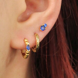 May include: Gold hoop earrings with blue gemstone accents. One hoop earring has a textured design.